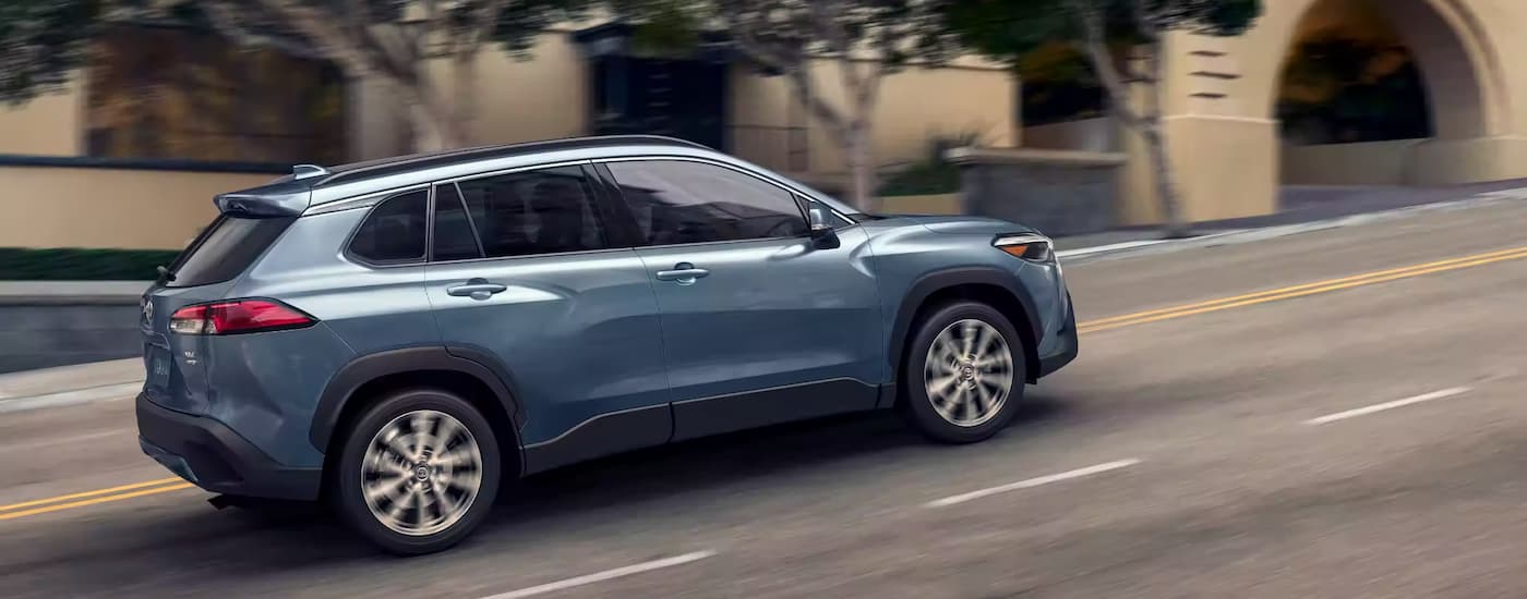 Side view of a blue 2023 Toyota Corolla Cross XLE AWD driving up a city street hill.