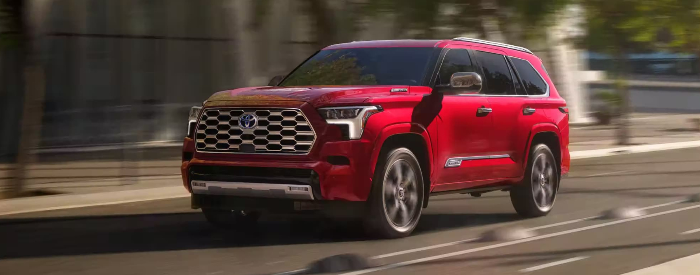 A red 2023 Toyota Sequoia Capstone driving on a city street near a used SUV dealer.