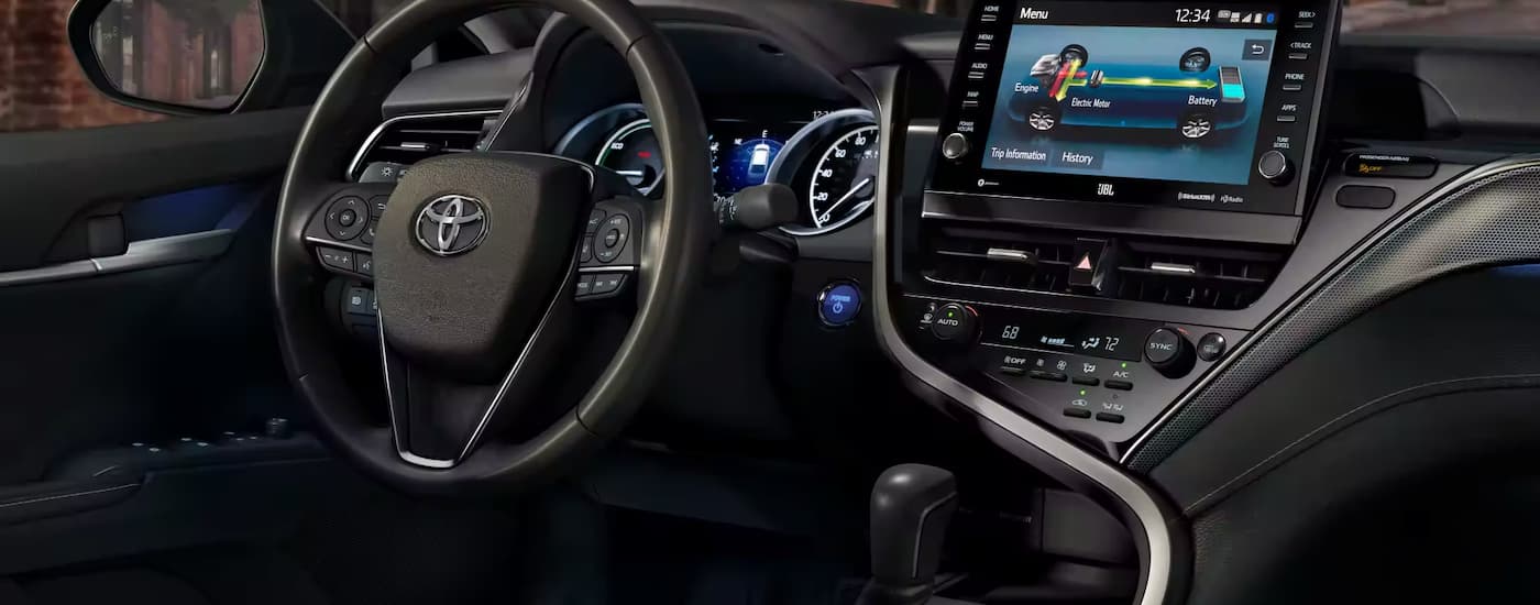The black interior of a 2023 Toyota Camry shows the steering wheel and infotainment screen.