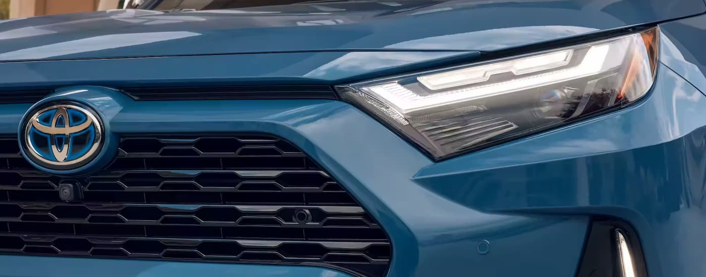 A close up of the grille and headlight on a blue 2023 Toyota RAV4 Hybrid XSE.
