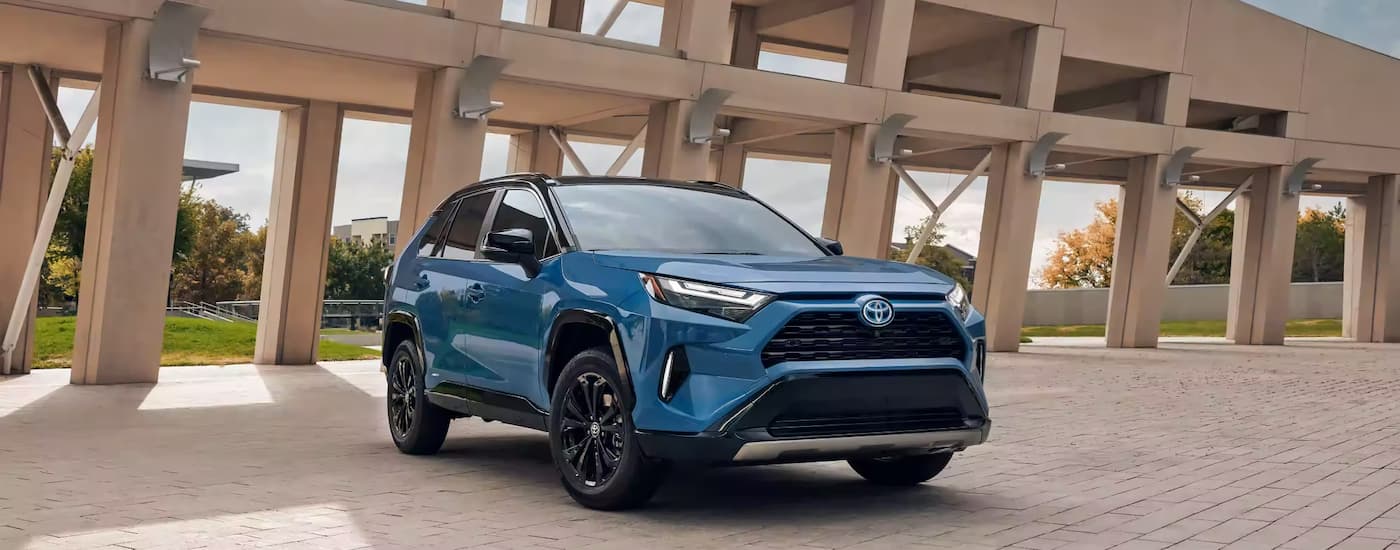 A blue 2023 Toyota RAV4 Hybrid SE parked near a concrete structure.