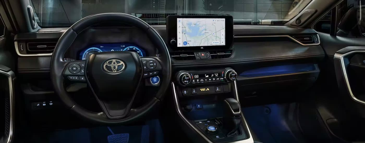 The black interior of a 2023 Toyota RAV4 shows the steering wheel and center console.