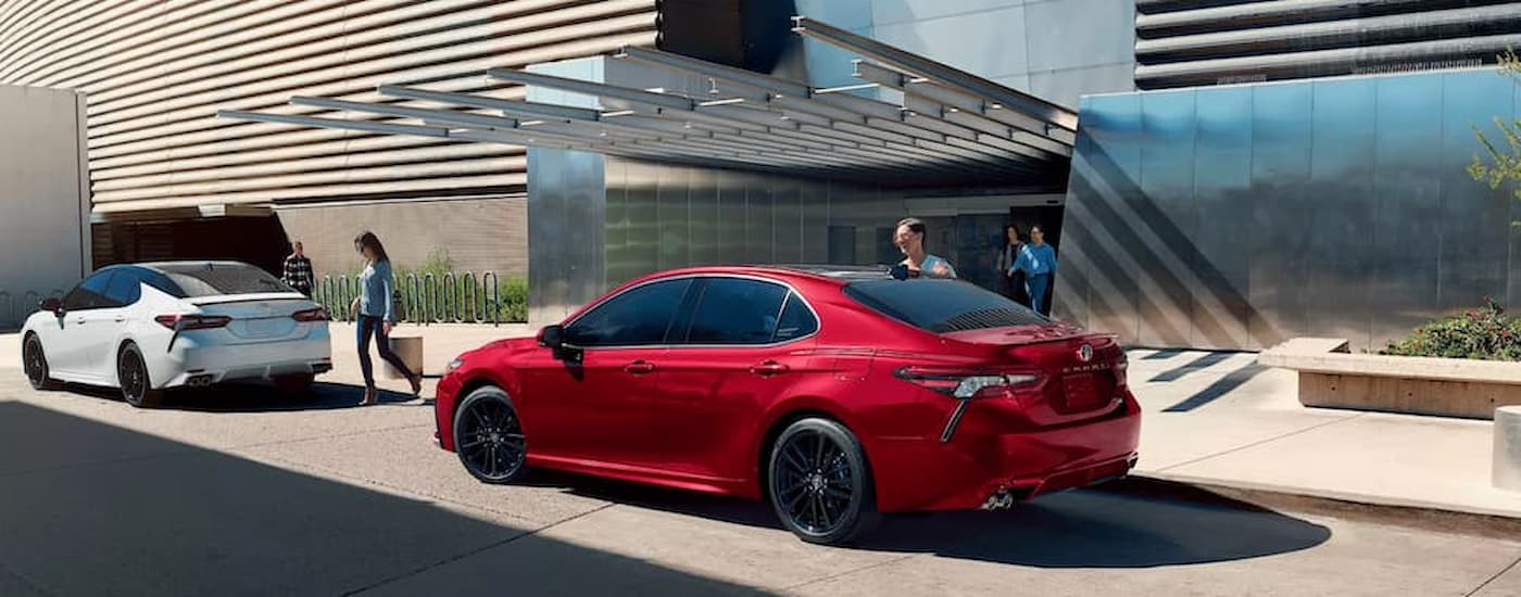Two 2022 Toyota Camrys, one red and one white, parked in front of a modern industrial building.