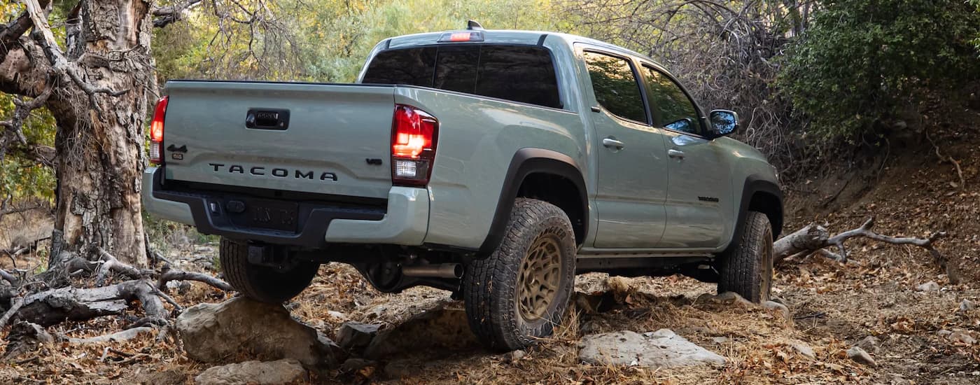 A grey 2022 Toyota Tacoma SR5 off-roading on a rocky trail in the woods.