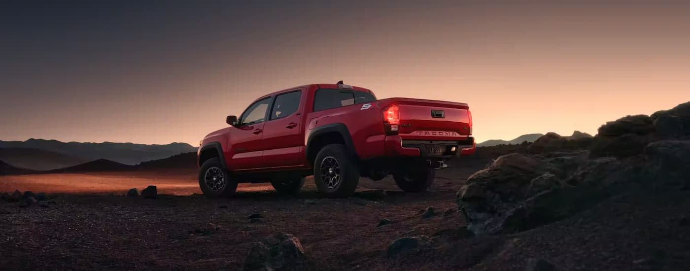 Seen from below, a red 2023 Toyota Tacoma is parked in an open desert during a sunrise.