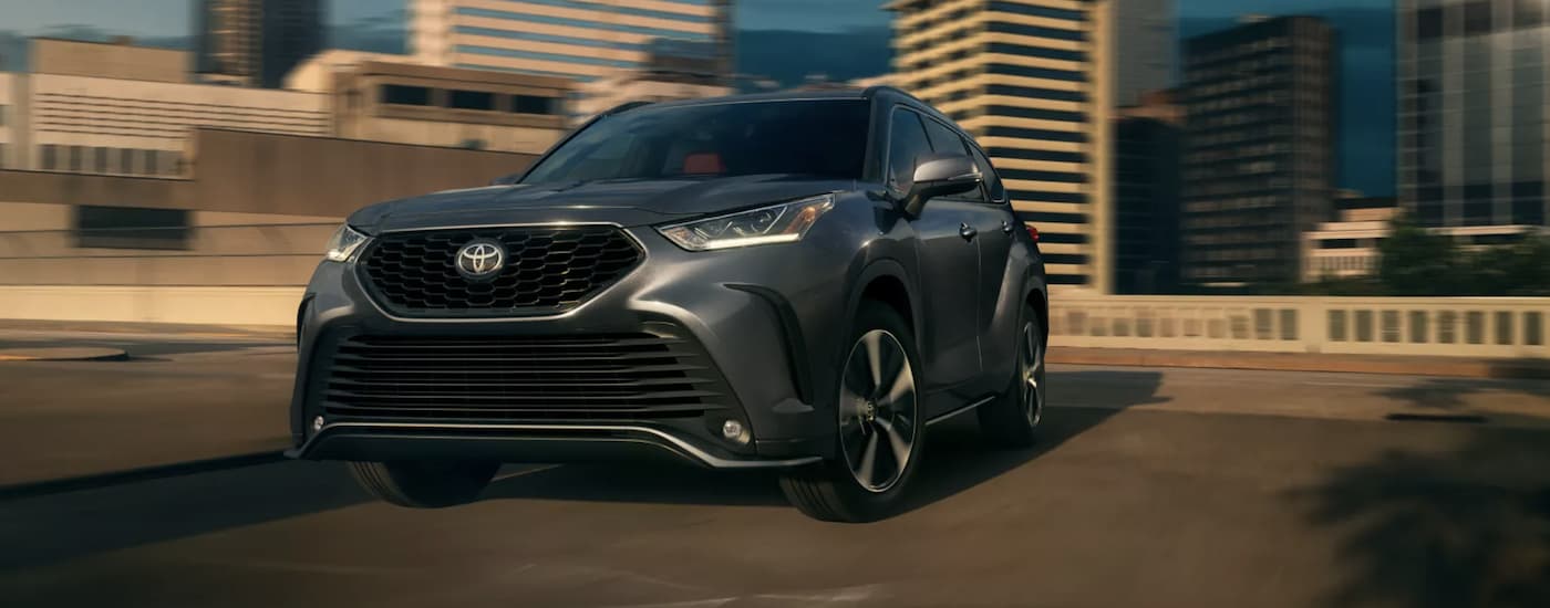 A grey 2022 Toyota Highlander XSE is shown from the front driving on an open road through a city.