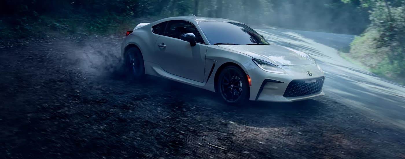 A white 2022 Toyota GR86 kicking up dust as it drives on a winding road
