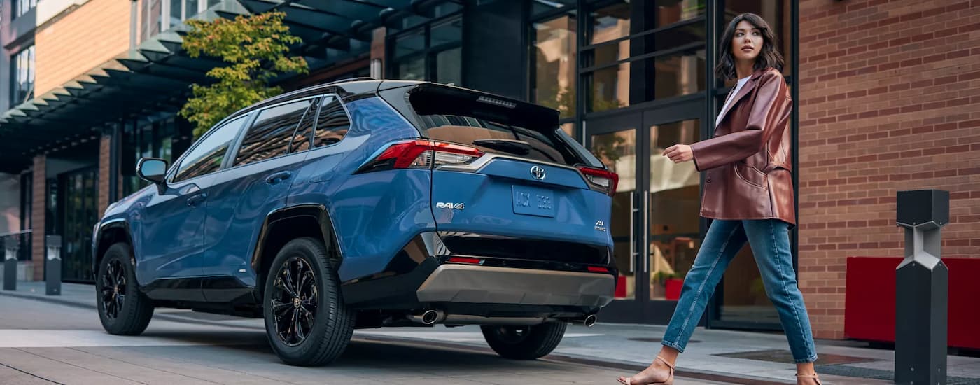 A woman is shown walking past a blue 2022 Toyota RAV4 XSE