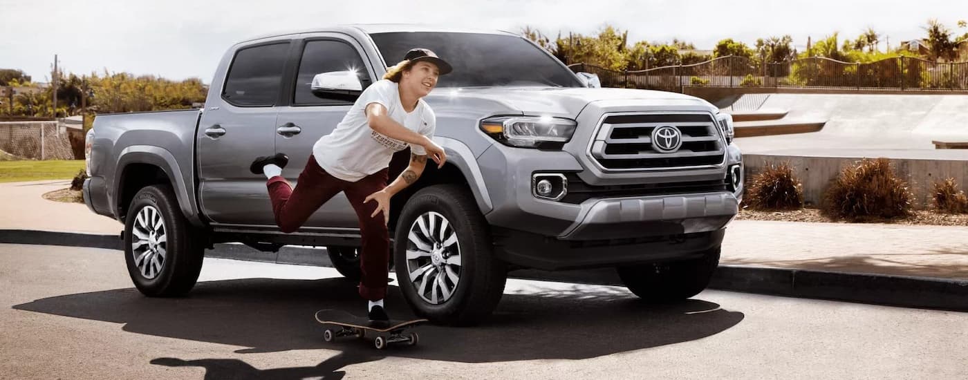 A skateboarder rolls by a silver 2022 Toyota Tacoma parked at a skate park.