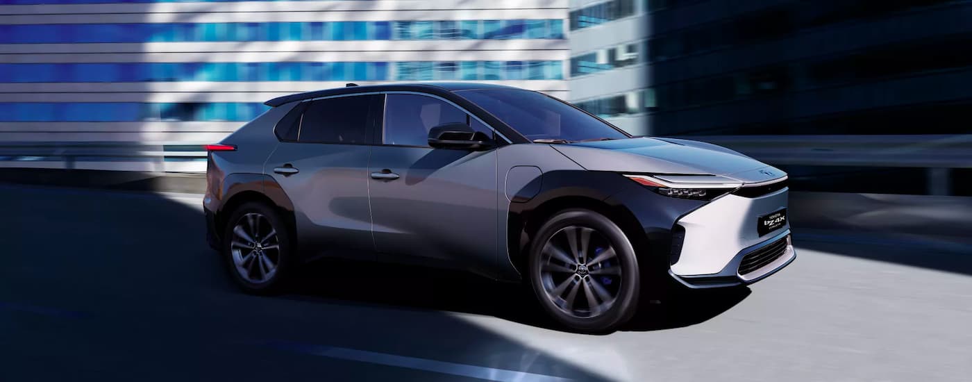 A grey 2022 Toyota bZ4X BEV driving past a city building.