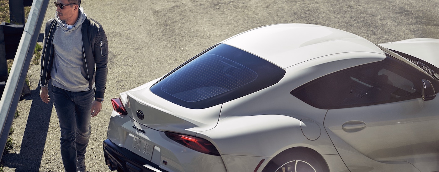 A man in jeans and a leather jacket walking past a white 2020 Toyota Supra GR.