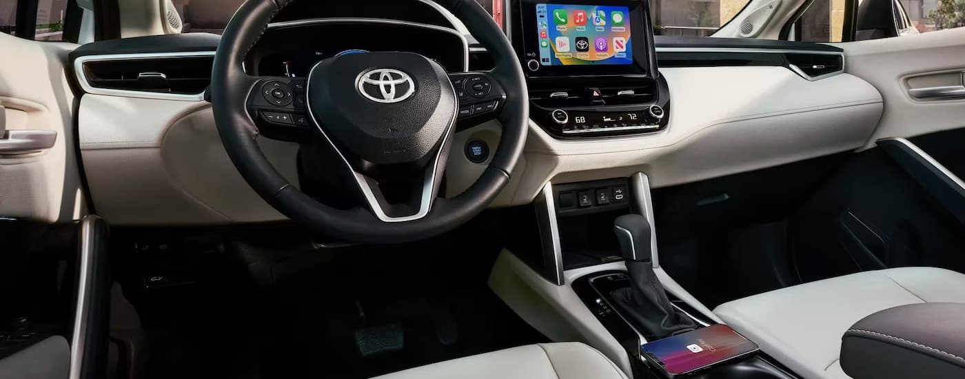 The black and tan interior of a 2023 Toyota Corolla Cross shows the steering wheel and center console.