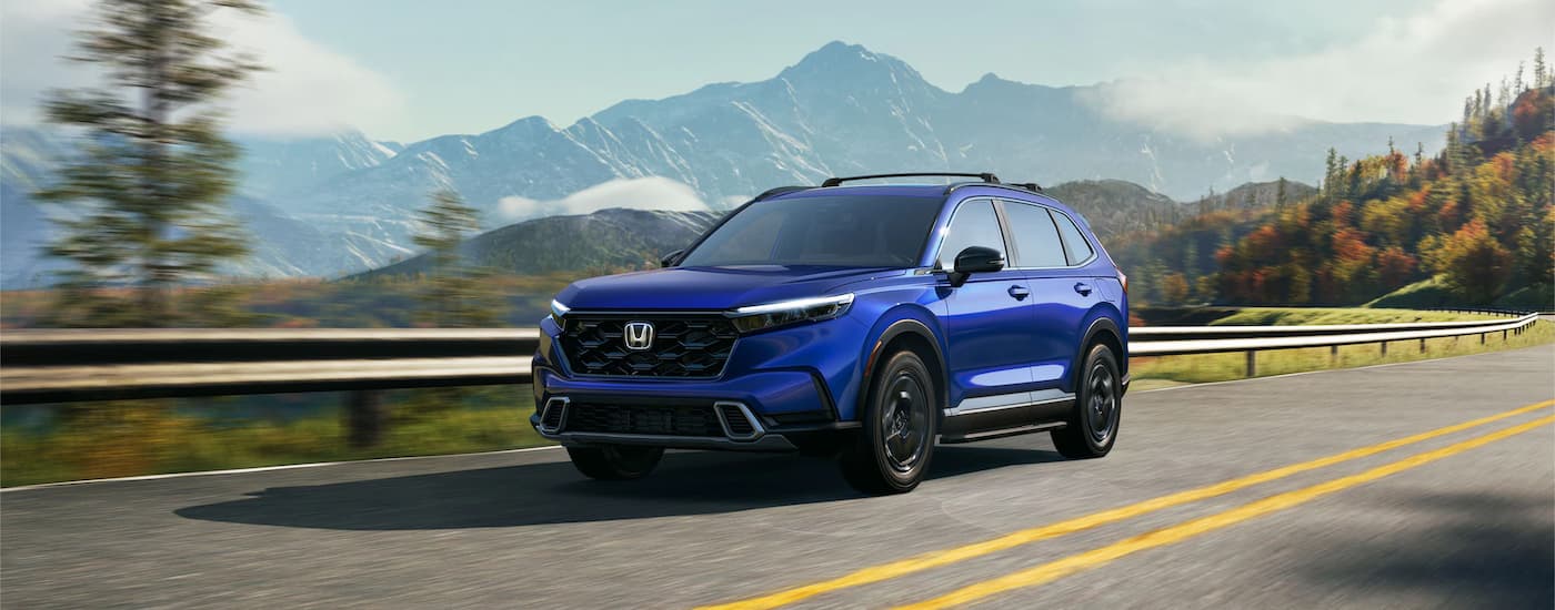 A blue 2023 Honda CR-V Sport Touring is shown driving on a mountain highway after visiting a Honda Dealer near Sacramento.