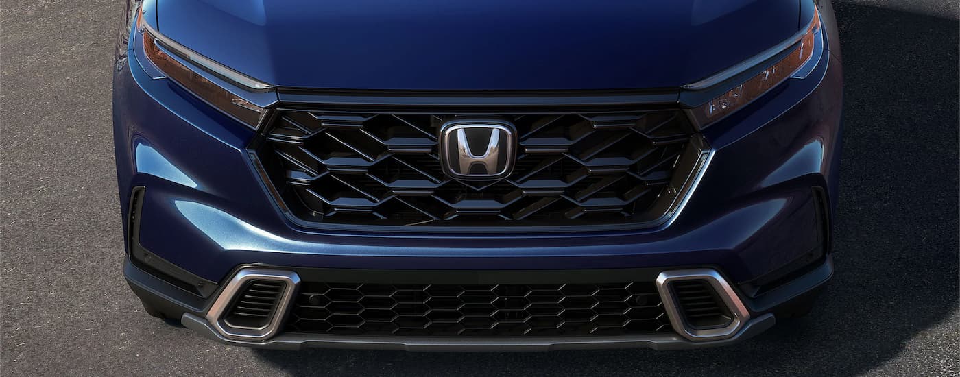 A close up of the grille of a blue 2023 Honda CR-V is shown on a paved parking area.