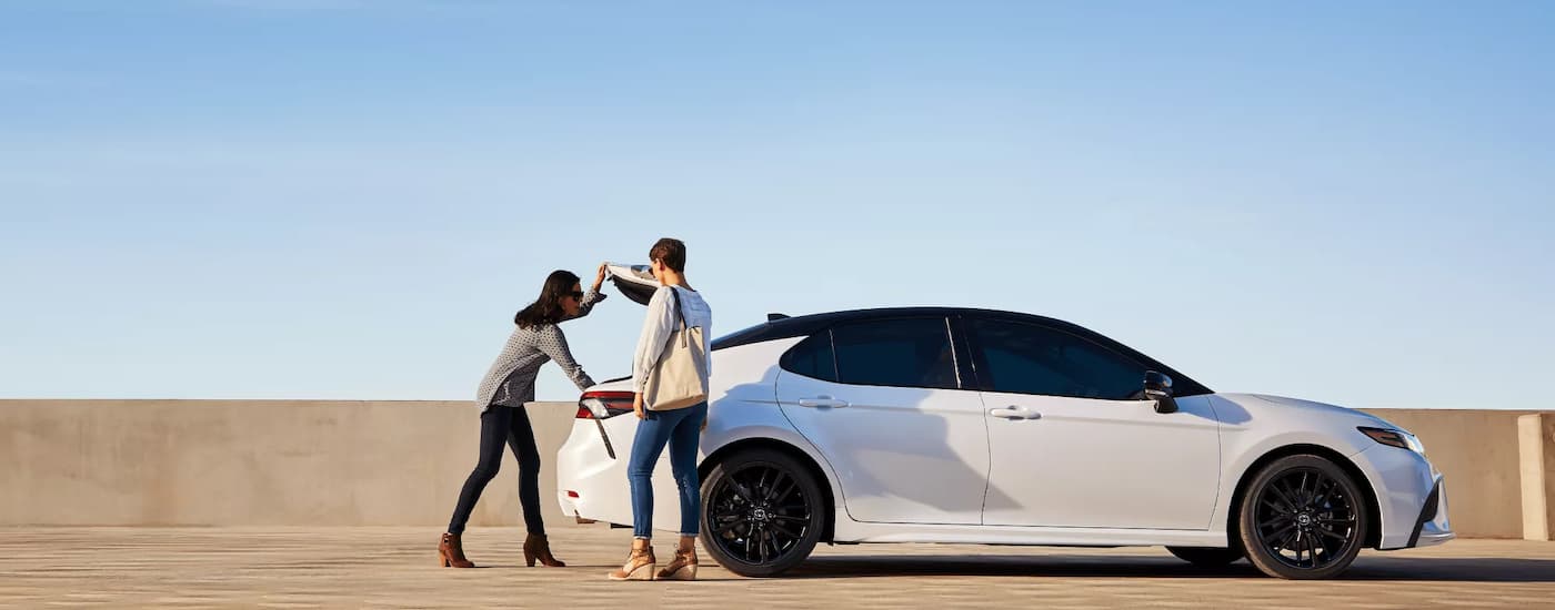 Two women accessing the trunk of a white Toyota Camry in an open parking lot