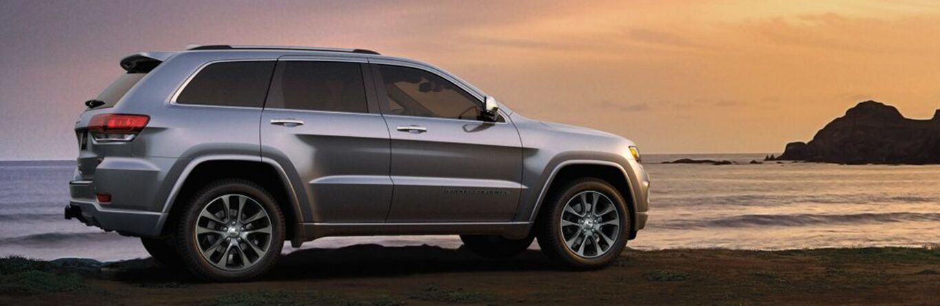 2019 Jeep Grand Cherokee silver exterior passenger side parked on beach at sunset