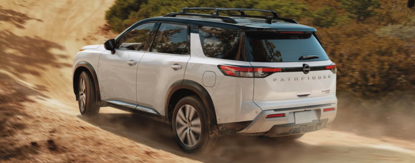 A popular Nissan Pathfinder for sale, a white 2023 Nissan Pathfinder, is shown from the rear driving on a dirt road.