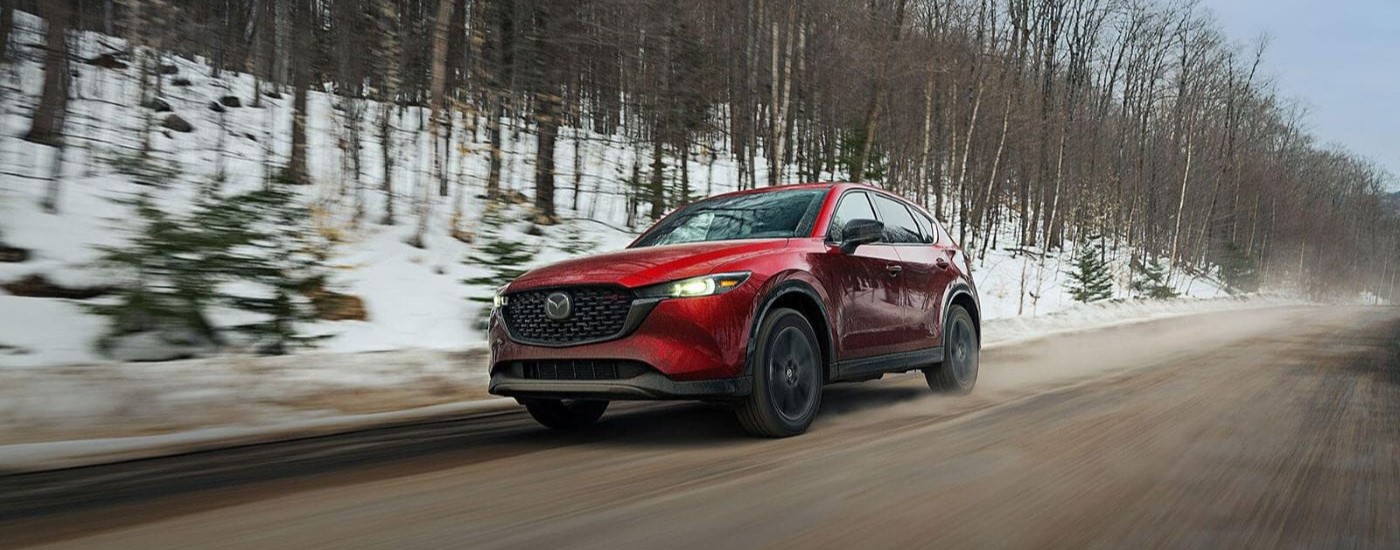 A red 2023 Mazda CX-5 for sale is shown driving on a dirt path.