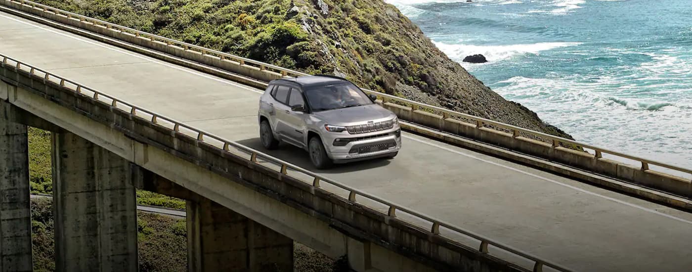 A grey 2022 Jeep Compass is shown driving over a bridge.