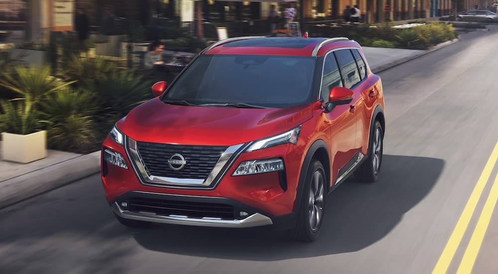 A red 2023 Nissan Rogue is shown from the front driving on an open road.