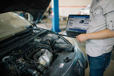 man looking under car hood with laptop