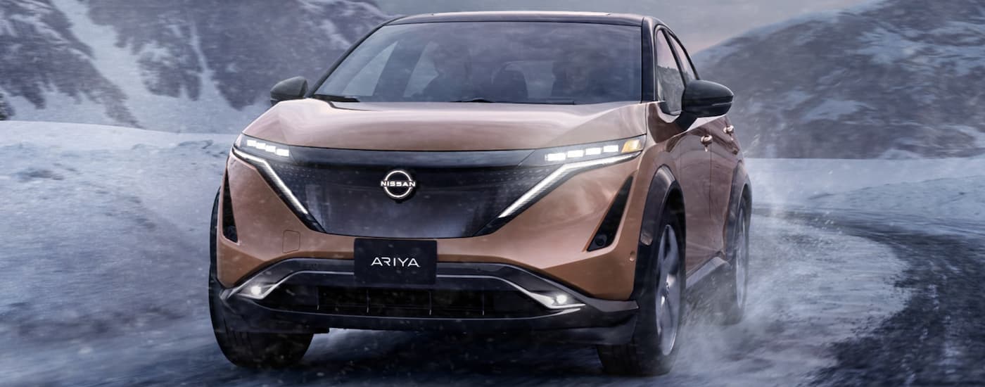A gold 2023 Nissan ARIYA is shown from the front driving in the snow.