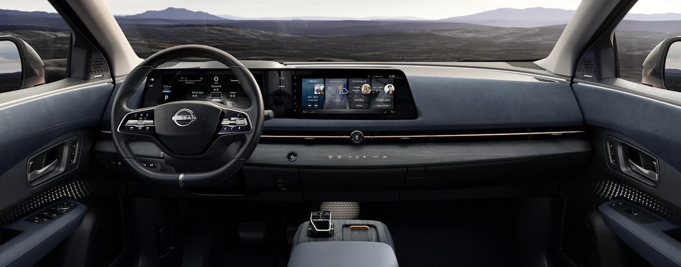 The black interior of a 2023 Nissan ARIYA shows the steering wheel and infotainment screen. 