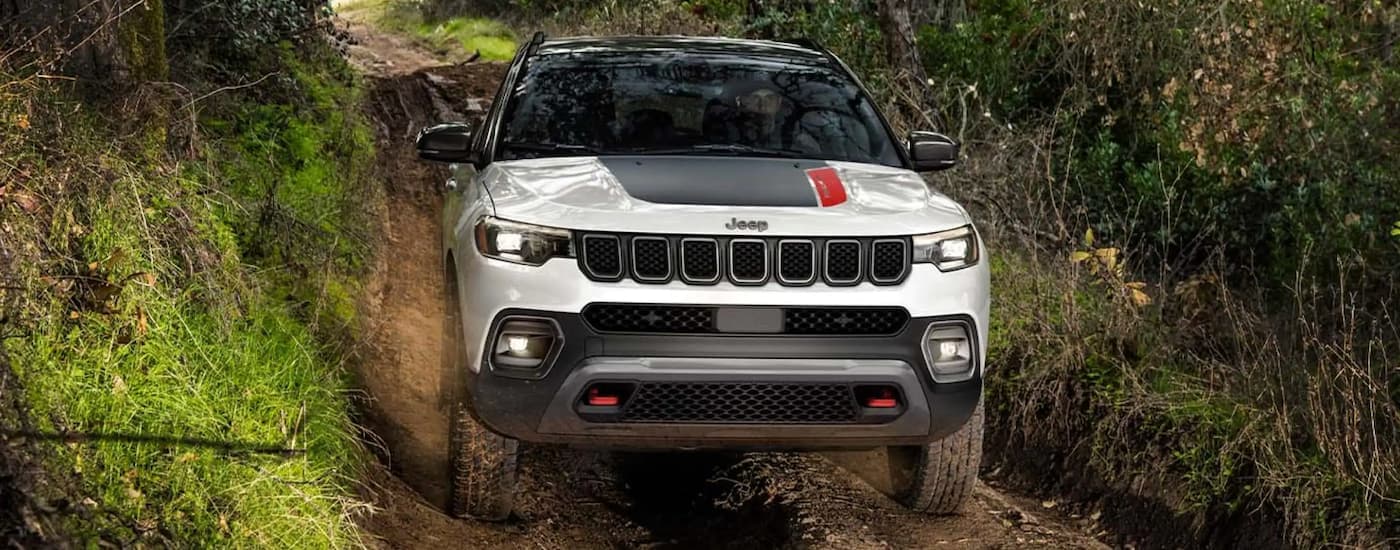 A white 2023 Jeep Compass is shown off-roading on a dirt road.