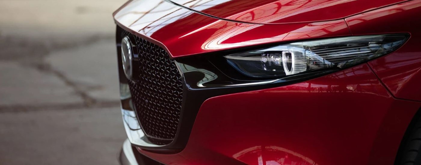 A close up shows the driver side headlight on a red 2023 Mazda3.