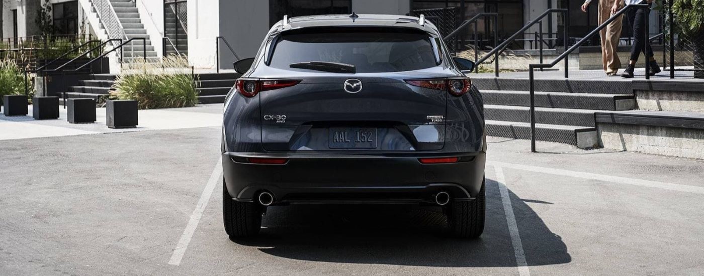 A grey 2023 Mazda CX-30 is shown from the rear parked in front of a building.