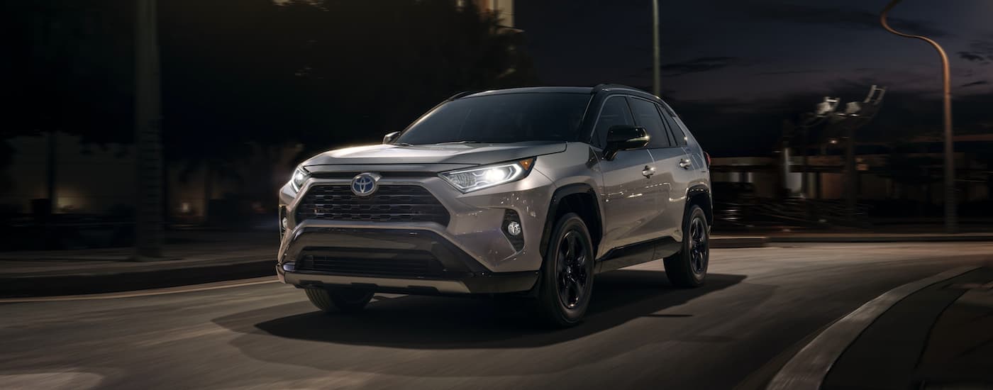 A silver 2020 Toyota RAV4 driving on a city street at night.