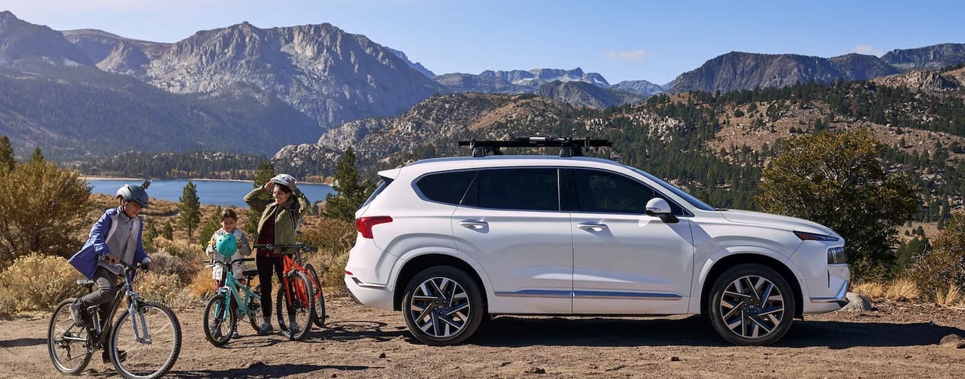 A white 2023 Hyundai Santa Fe is shown from the side parked next to bikers.