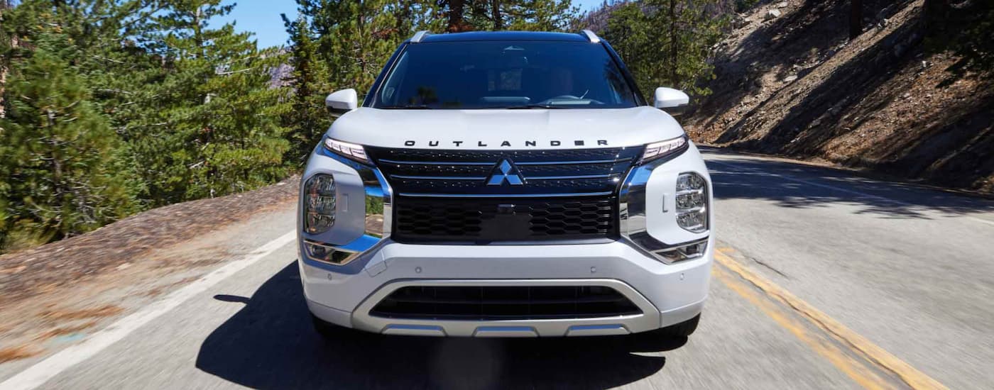 A white 2023 Mitsubishi Outlander PHEV is shown from the front driving on an open road.