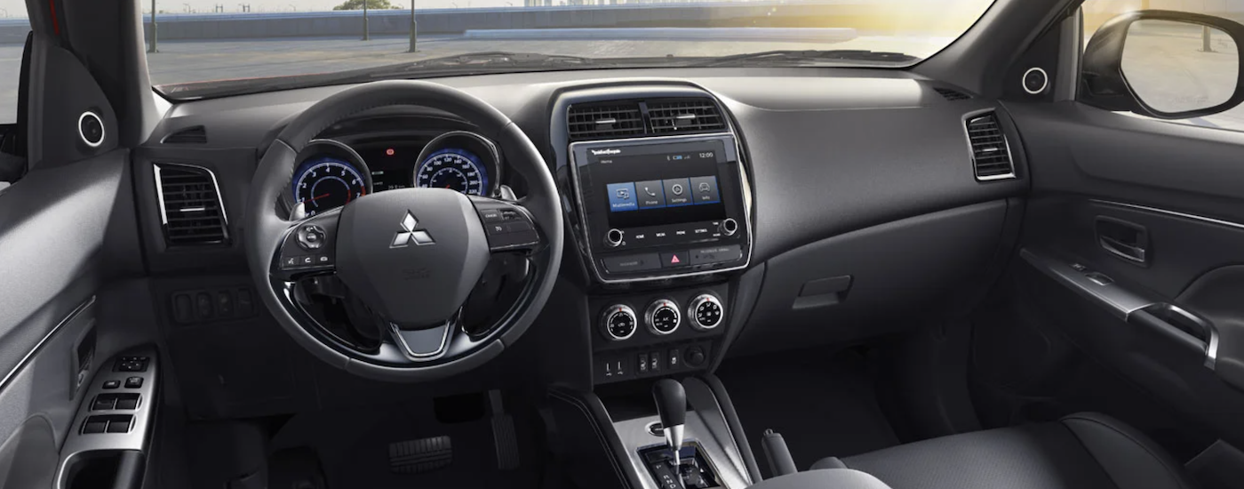The black interior of a 2023 Mitsubishi RVR shows the steering wheel and infotainment screen.