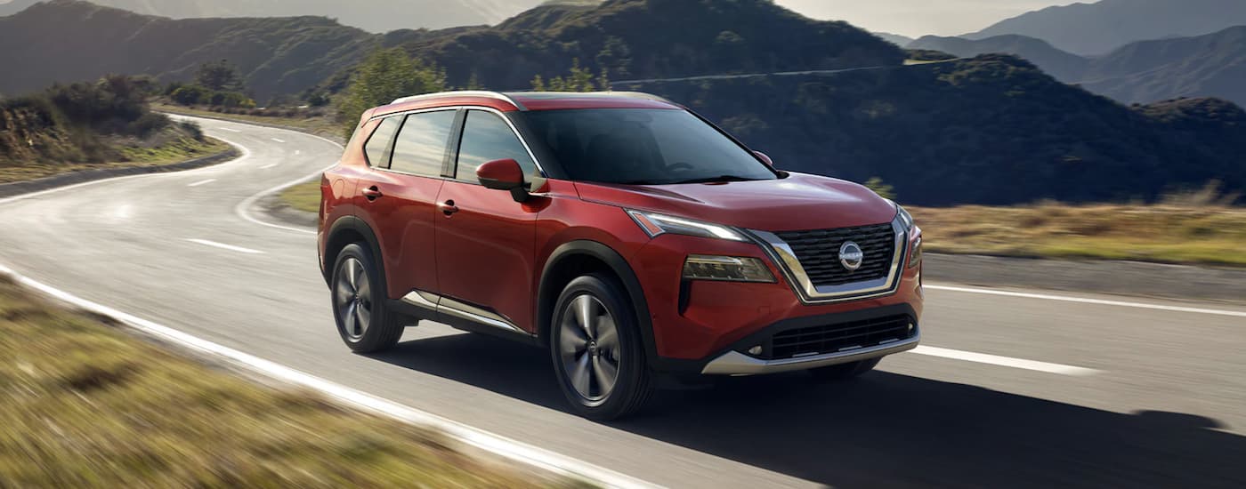 A red 2023 Nissan Rogue is shown on a winding road.