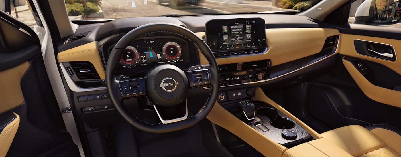 The black and yellow interior of a 2023 Nissan Rogue shows the steering wheel and infotainment screen.