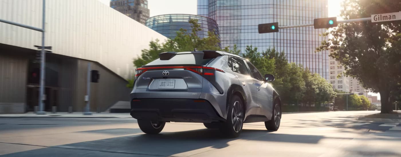 A silver 2023 Toyota bZ4X is shown from the rear driving on a city street.