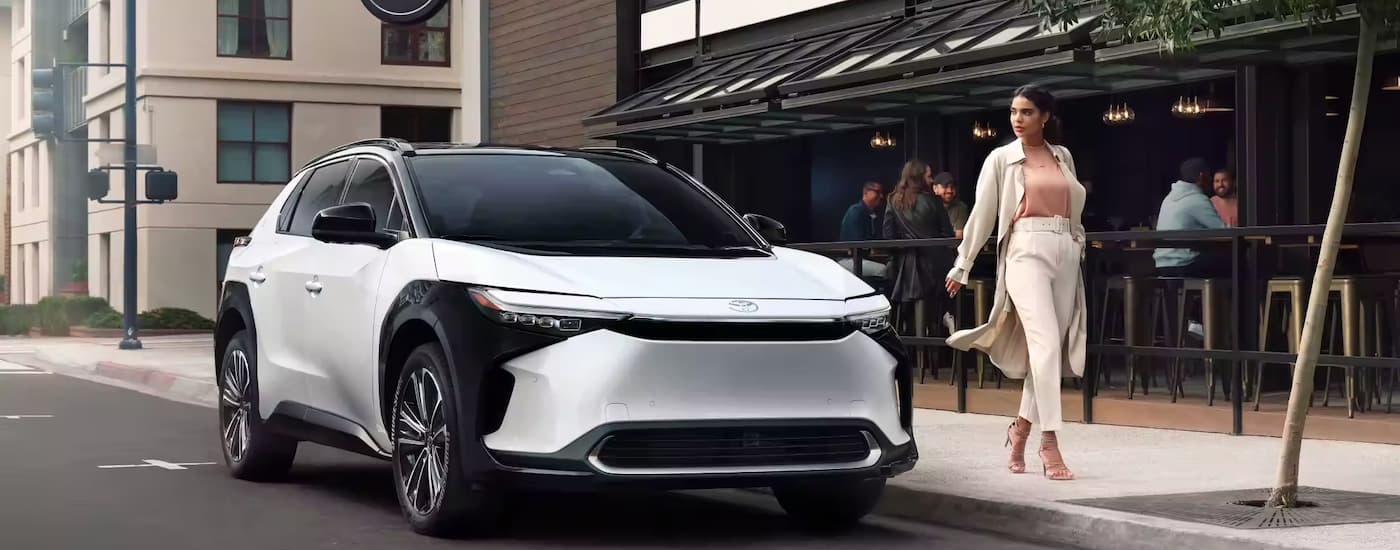 A white 2023 Toyota bZ4X is shown parked on the side of a city street near a bar.