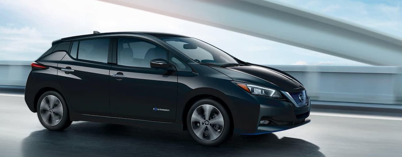 A black 2023 Nissan Leaf for sale is shown driving on a highway during a test drive.