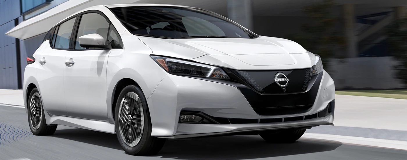 A white 2023 Nissan Leaf for sale is shown driving on a city street.