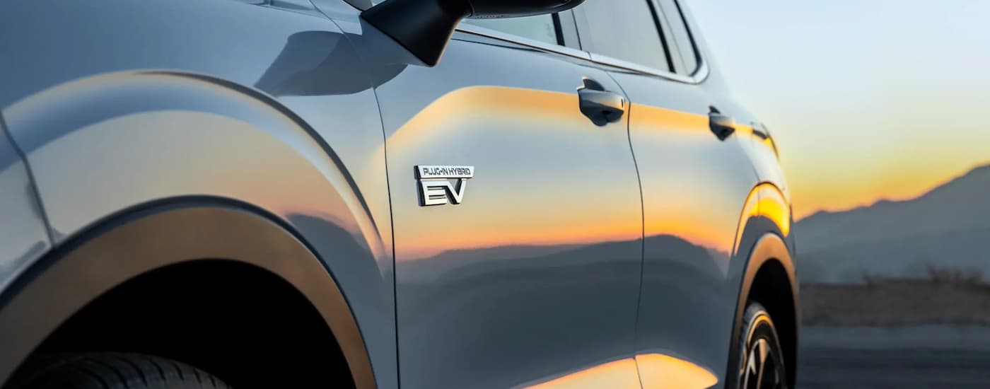 A close up of the side of a grey 2023 Mitsubishi Outlander PHEV is shown during a sunset.