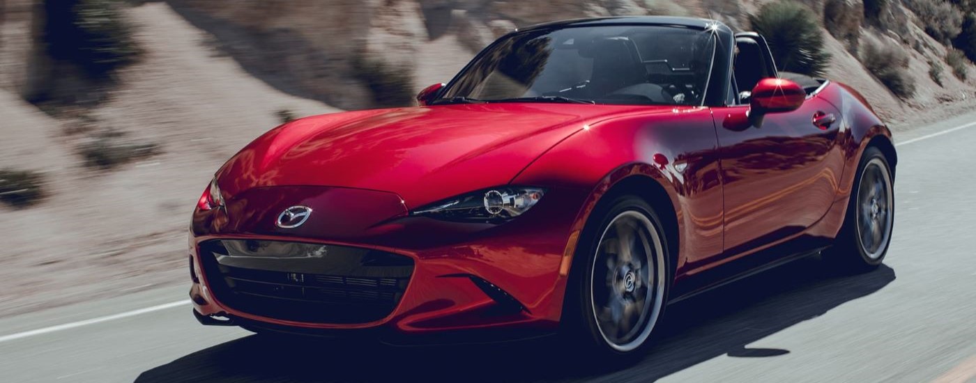 A red  2019 Mazda MX-5 Miata is shown driving on an open road.