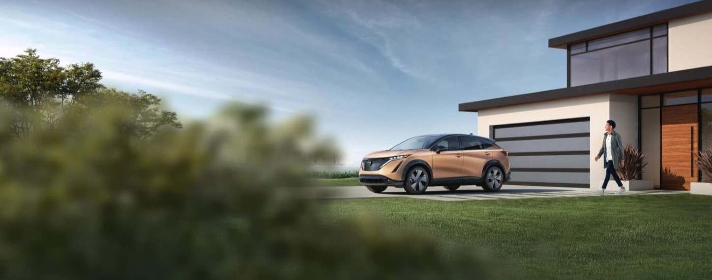 A bronze 2023 Nissan Ariya is shown on a driveway after looking at electric vehicles for sale.