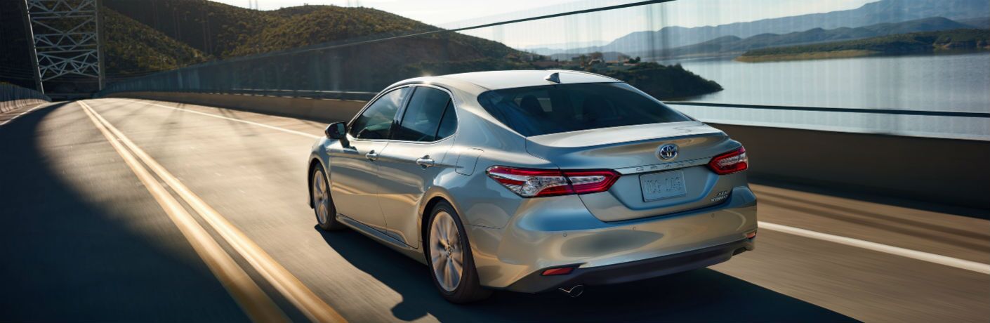 Silver 2020 Toyota Camry drives on a highway alongside a body of water.