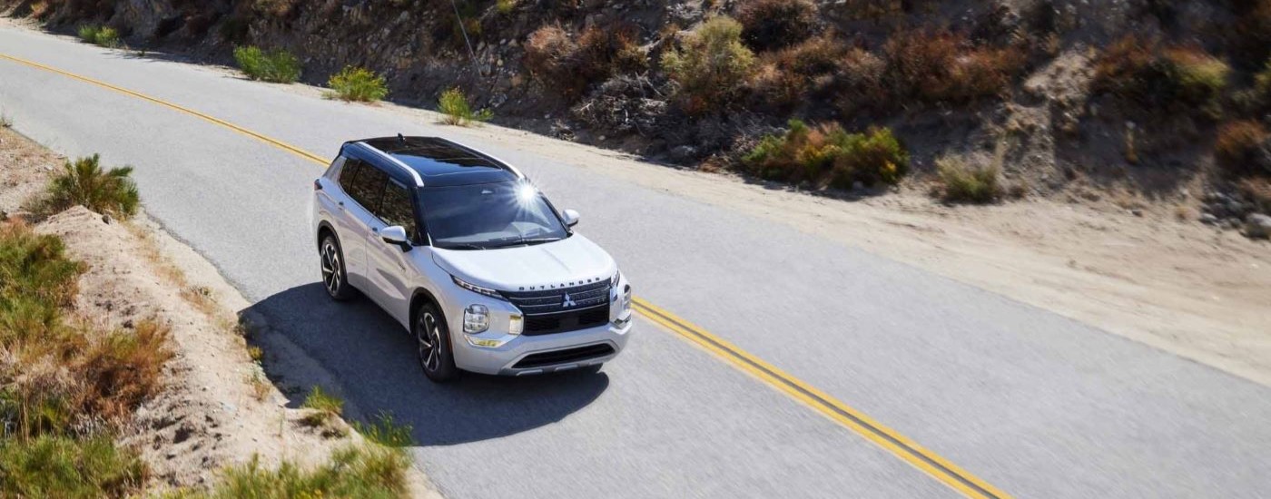 A white 2023 Mitsubishi Outlander PHEV is shown on an open road after looking at electric vehicles for sale in Edmonton.