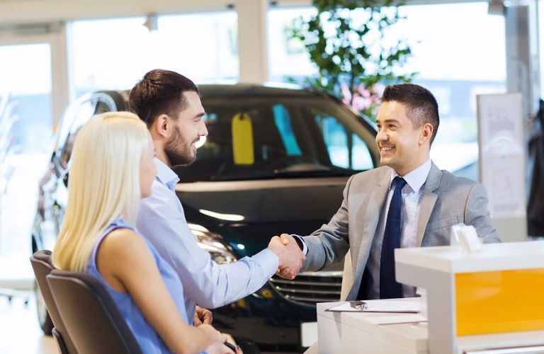 A salesman shakes the hand of a customer who sits beside a woman. Both seem satisfied with the …