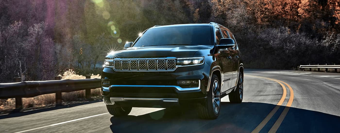 A black 2023 Grand Wagoneer for sale is shown driving on a winding road.