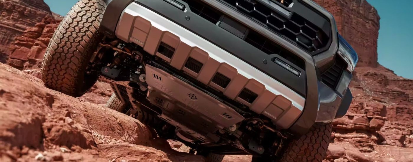 A popular Toyota Tacoma for sale, a green 2024 Toyota Tacoma Trailhunter, is shown crawling over rocks.