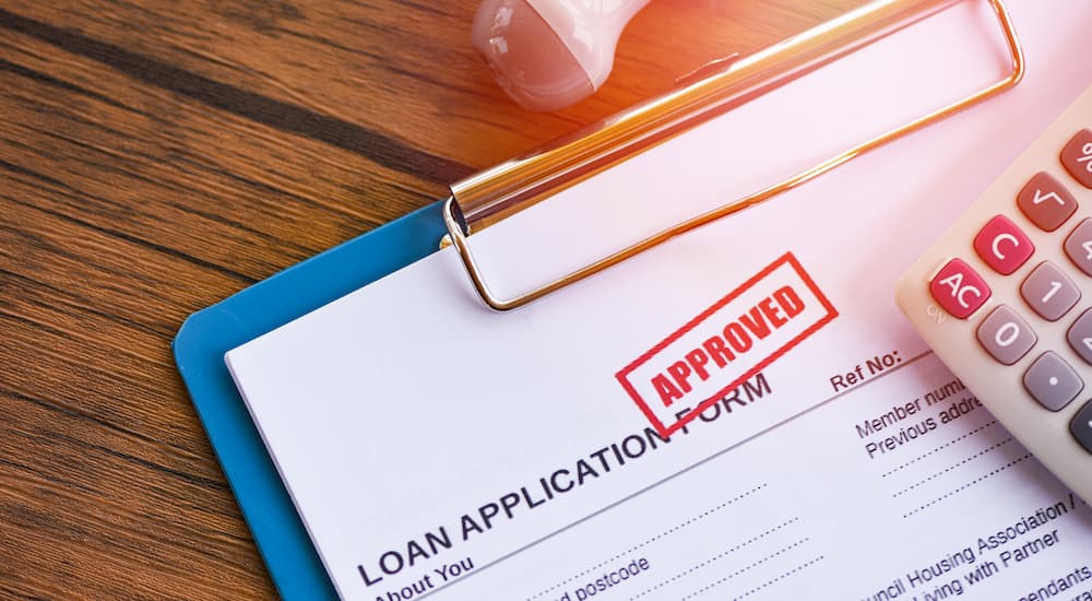 An approved bad credit car loan is shown on a blue clipboard.