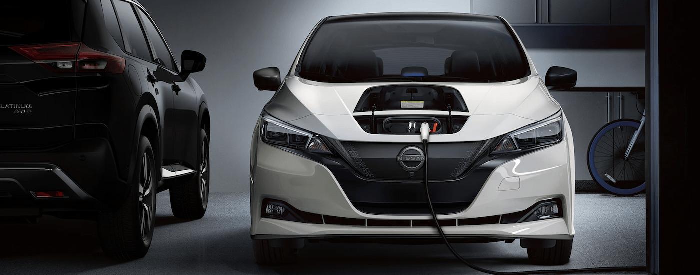 A white 2023 Nissan Leaf is shown from the front parked in a garage while charging.